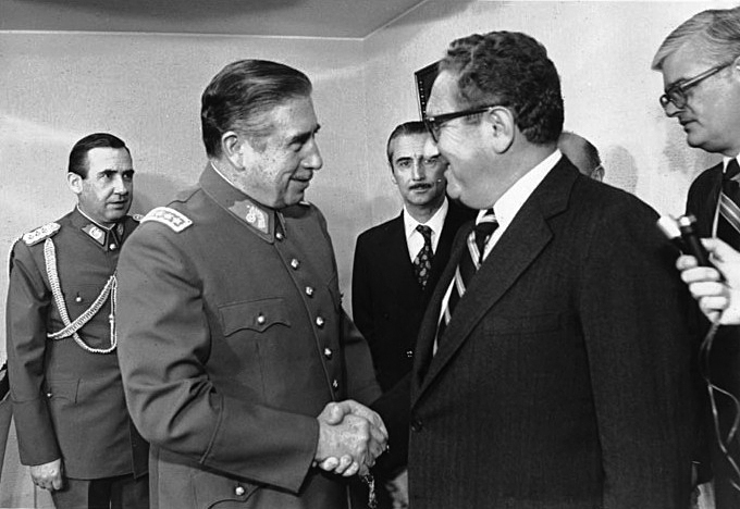 Foto van de oorlogscrimineel Kissinger en de Chileense dictator Pinochet, ze schudden handen.