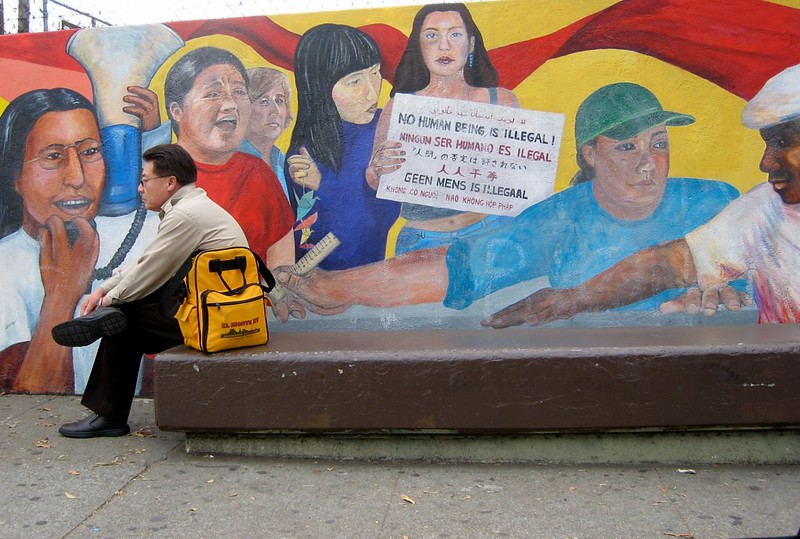 muurschildering met mensen met verschillende huidskleuren en de tekst 'geen mens is illegaal' in meerdere talen